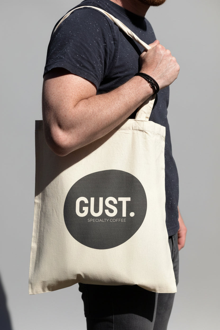 Person holding a beige tote bag with 'GUST.' logo against a dark background